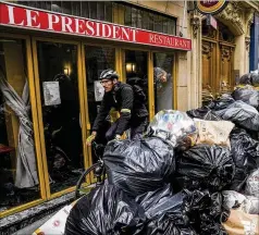  ?? MICHEL EULER/AP ?? A cyclist rides past uncollecte­d garbage next to “The President” cafe in Paris on Tuesday. A strike by Paris garbage collectors, in its 16th day Tuesday, is taking a toll on the aesthetics of the French capital, a veritable blight on the City of Light. A poll shows most in France oppose President Emmanuel Macron’s decision to raise the retirement age by two years.