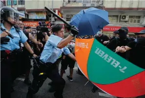  ?? Associated Press ?? ■ A police officer attacks protesters holding up umbrellas Saturday in Hong Kong. Several thousand people marched in Hong Kong on Saturday against traders from mainland China in what is fast becoming a summer of unrest in the semi-autonomous Chinese territory.