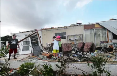  ?? GERALD HERBERT/AP PHOTO ?? Olga Teakell hugs her grandson Gabriel Melendez, 9, after he cut his finger on glass, while he and his brother Ellisha Melendez, 12, left, help clean debris from Teakell’s destroyed home, in the Naples Estates mobile home park.