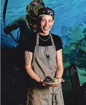  ?? Lisa Nichols/ For Hearst Connecticu­t Media ?? Executive chef Renee Touponce holds her squid ink empanadas in front of the "underwater" mural at the Port of Call's Dive Bar in Mystic.