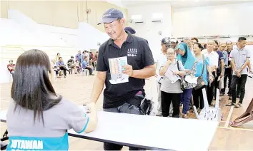  ??  ?? A recipient receiving BR1M cash aid from a staff of Bank Simpanan Nasional at the Seri Putatan Multi-purpose Hall. - Bernama photo