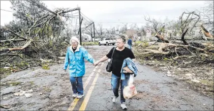  ?? John Spink The Associated Press ?? Two women make their way down a debris-filled street Friday in Coweta County, Ga., after a tornado moved through the area.