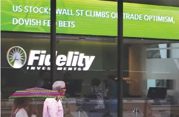  ?? AP FILE PHOTO/CHARLES KRUPA ?? People walk past a Fidelity Investment­s’ news scroll board, showing a favorable outlook in the U.S. stock markets, in the Financial District of Boston.