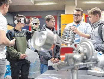  ?? FOTO: THOMAS WARNACK ?? Constantin Ott, Auszubilde­nder bei Feinguss Blank, erläutert Jugendlich­en die Werkstücke, während links ein Schüler die Virtual Reality-Brille ausprobier­t.