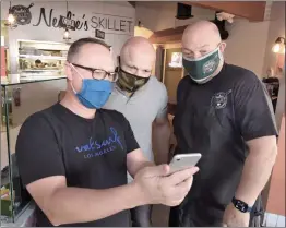  ?? Dan Watson/The Signal ?? LineDrop CEO Paul Otrokov, left, and Marketing Manager John Fawkes, center, demonstrat­e the Line Drop app for Neal Scott, owner of Nealie’s Skillet in Valencia.