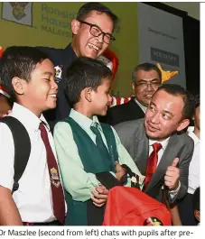  ??  ?? Dr Maszlee (second from left) chats with pupils after presenting them with new school uniforms, shoes and bags for the upcoming school year while Azmir (left) looks on.