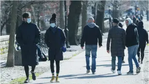  ?? (Andrew Kelly/Reuters) ?? PEOPLE IN SURGICAL masks walk along a path around Prospect Park in Brooklyn, Sunday.