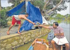  ?? AP ?? A flood affected man, left, sends a bank passbook through a boatman so that his family, which has taken refuge in a relief camp, can apply for aid from the government in Alappuzha, Kerala, on Monday.