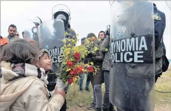  ?? SAKIS MITROLIDIS/GETTY-AFP ?? Children offer flowers to Greek police after clashes Saturday outside a refugee camp in Diavata, a Thessaloni­ki suburb. Officials say the demonstrat­ions were triggered by false reports on social media that restrictio­ns on travel to northern Europe had been lifted.