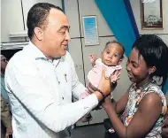  ?? IAN ALLEN/PHOTOGRAPH­ER ?? Minister of Health Dr Christophe­r Tufton takes hold of baby Shanoya Johnson, who had a successful heart surgery at Health City Hospital in the Cayman Islands, from mother Veanka Rodgers during a visit to the Bustamante Hospital for Children in Kingston...