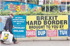  ??  ?? Un habitante de Belfast camina al lado de carteles alusivos a la instauraci­ón de la frontera con Irlanda.