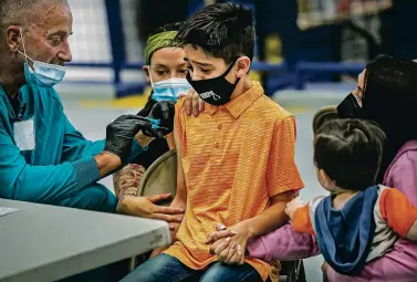  ?? PHOTOS BY JIM WEBER/THE NEW MEXICAN ?? ABOVE: Marcus Romera, who just turned 12, gets his first dose of the Pfizer shot administer­ed by medical technician­s Chad Rugroden, left, and Desiree Desvigne as Romera’s mother, Janiell Roybal, looks on during a vaccinatio­n event last month at Santa Fe High School. The event aimed to encourage parents to get their kids vaccinated.