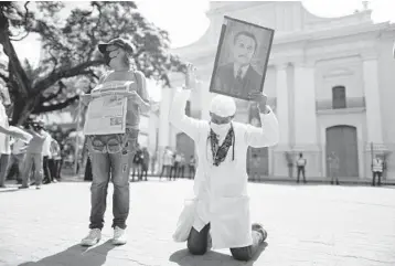  ?? ARIANA CUBILLOS/AP ?? A step closer to sainthood: Yeni Vasquez holds a portrait of Dr. Jose Gregorio Hernandez, a man revered by millions of Venezuelan­s as the “doctor of the poor,” on Friday outside a church in Caracas, Venezuela. Hernandez, who died in 1919, moved one step closer to sainthood after being beatified in a simple ceremony aired live on national television.
