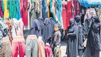  ?? ?? Women walk past a garment shop at the al-Hol camp.