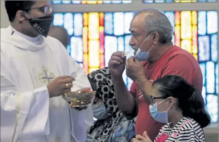  ?? ERIC GAY / AP ?? The Rev. Praveen Lakkisetti­t, left, wears a face mask as he delivers communion to parishione­rs during an in-person Mass at Christ the King Catholic Church in San Antonio, Tuesday.