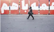  ?? ?? A woman walks past a banner reading “All together for homeland” in Tehran, Iran, March 4, 2024.