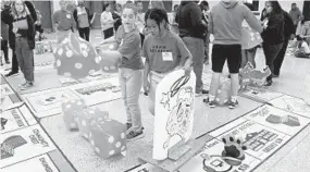  ?? KIM HAIRSTON/BALTIMORE SUN ?? From left, Sienna Vickerie, 11, and Donte Edmunds, 10, members of the Federal Hill Preparator­y School Brain Breakers team, move their game piece on a large Mathopoly game board.