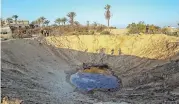  ?? (AFP) ?? Palestinia­ns gather around a crater caused by an Israeli airstrike, in Khan Yunis in the southern Gaza Strip on Saturday