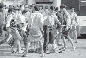  ?? GETTY-AFP ?? Violence in Myanmar: Pro-military supporters, including one brandishin­g a knife, left, stand over an anti-coup demonstrat­or after attacking him Thursday in Yangon, Myanmar. The violence complicate­s a standoff between the military and a protest movement that has been staging rallies daily to demand that the elected government be restored to power.