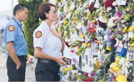  ?? DAVID SANTIAGO/MIAMI HERALD ?? Miami-Dade Fire Rescue personnel Fai Yeung, left, and Chief Melanie C. Adams visit the makeshift memorial setup near the partially collapsed 12-story Champlain Towers South Condo on Thursday in Surfside, Florida.