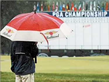  ?? TONY GUTIERREZ/AP ?? A fan braves the elements near the 18th hole after third-round play was suspended for the day at the PGA Championsh­ip.