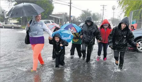  ??  ?? PEDESTRIAN­S cross a f looded intersecti­on on Gloria Avenue in Van Nuys. The storm arrived with strong gusts and bursts of heavy rain, a potent combinatio­n that at one point Friday evening had more than half a dozen major freeways and highways around...