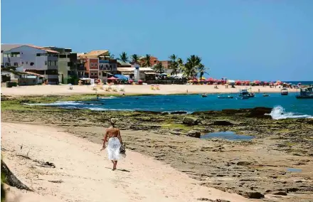  ??  ?? Mulher caminha por praia próxima ao centro do vilarejo de Arembepe, reduto hippie a 42 quilômetro­s de Salvador