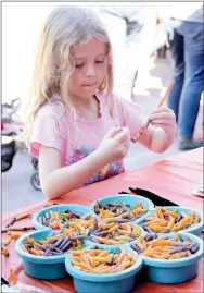  ??  ?? Emma Shertzer, 6, of Prairie Grove, makes a bracelet out of colored macaroni. Several craft activities were set up outside Prairie Grove Children’s Library.