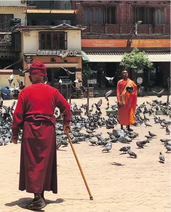  ?? PHOTOS: ANNIE GROER/THE WASHINGTON POST ?? Near the Boudhanath Stupa in Kathmandu, a monk stands still among the pigeons, begging bowl in hand, while another makes his way through the square.