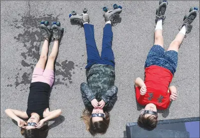  ?? (NWA Democrat-Gazette/Andy Shupe) ?? Ellie Hammer (from left), 9; Liam Hammer, 11; and Dagan Crider, 10, lie on their backs Monday while watching the solar eclipse at the Arkansas Air and Military Museum in Fayettevil­le. The museum partnered with Starlight Skatium, which debuted its new mobile skating rink for the free event. Visit nwaonline.com/photo for today’s photo gallery.