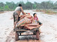  ??  ?? MUD IN YOUR EYE: Flood victims transport their belongings along a muddy road in Attapeu province. Rescuers battled fresh rains on July 26 to reach scores of people.