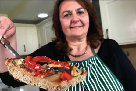  ?? The Associated Press ?? Tiziana di Costanzo, co-founder of Horizon Insects, holds up a slice of pizza made with cricket powder, in her London kitchen.