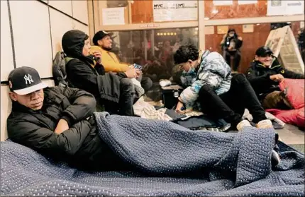  ?? Jeenah Moon / The New York Times ?? Migrants rest on the ground at the Watson Hotel in Manhattan as a protest against being sent to a shelter at a cruise ship terminal in Brooklyn. New York City has franticall­y sought to uphold its promise of shelter for all. But as more people arrive, services are being stretched past their capacity.