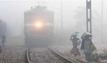  ?? — AFP ?? Women walk along a track as a train waits amid heavy fog and air pollution at Sahibabad station in Ghaziabad, some 25km east of New Delhi, on Monday.