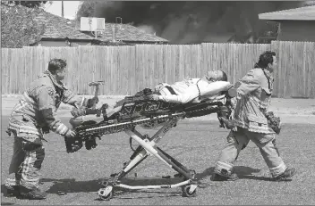  ??  ?? ABOVE: YFD emergency personnel transport a man from the scene of the fire early Thursday afternoon as flames rise in the backyard of the home.
LEFT: Yuma Police Department and YFD personnel, seen here in the alley between 8th Avenue and 9th Avenue, between 5th Street and 6th Street, work the scene of the fire.