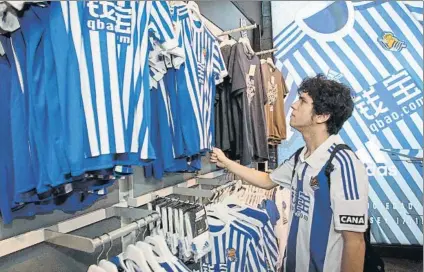  ?? FOTO: UNCITI ?? Un aficionado observa la camiseta de la Real de la que acabará desapareci­endo la publicidad de Qbao