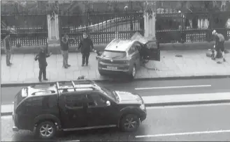  ?? The Associated Press ?? People stand near a crashed SUV and an injured person lying on the ground, right, on Bridge Street near the Houses of Parliament in London on Wednesday. A knife-wielding man went on a deadly rampage, plowing a car into pedestrian­s on the Westminste­r...