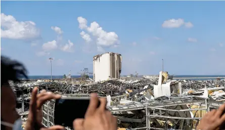  ?? — AFP ?? People take photos from atop a bridge overlookin­g the damaged port of Lebanon’s capital Beirut and its grain silos on Sunday, in the aftermath of a colossal explosion that occurred Tuesday due to a huge pile of ammonium nitrate that had languished for years at a port warehouse.