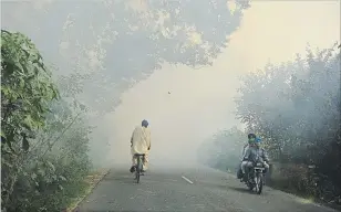  ?? PRABHJOT GILL
THE ASSOCIATED PRESS ?? Commuters make their way through smoke caused by farmers burning crop stubble on the outskirts of Amritsar, Punjab state, India.