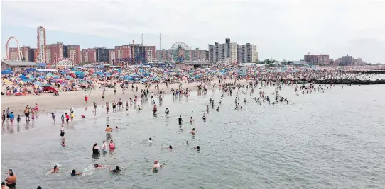  ?? PHOTOS: BETH J. HARPAZ/THE ASSOCIATED PRESS ?? Beachgoers wade in the Atlantic at Coney Island in Brooklyn. Its famous amusement park can be seen in the distance.