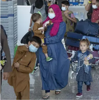  ?? Ap; leFt, getty images ?? WELCOME TO AMERICA: Families evacuated from Kabul, Afghanista­n, walk through the terminal to board a bus after they arrived at Washington Dulles Internatio­nal Airport in Chantilly, Va., on Saturday. At left, Taliban Badri fighters, a ‘special forces’ unit, stand guard as Afghans wait at the main entrance gate of Kabul airport to leave Afghanista­n on Saturday.