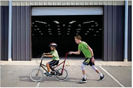  ?? NICK WAGNER/AMERICAN-STATESMAN ?? Volunteer Zac Hays helps Santiago Carrillo maneuver a bike during a Down Syndrome Associatio­n of Central Texas bike camp Aug. 3.