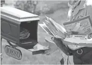  ?? TREVOR HUGHES/ USA TODAY ?? USPS carrier Amy Bezerra loads mail into a mailbox in suburban Denver along her route. A cloth mask dangles around her neck in case she needs to get close to people.