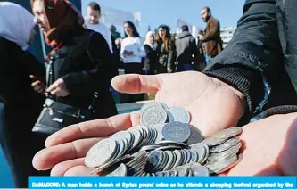  ?? —AFP ?? DAMASCUS: A man holds a bunch of Syrian pound coins as he attends a shopping festival organized by the Damascus Chamber of Industry in support of the local currency, in the Syrian capital Damascus yesterday.