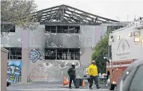  ?? ERIC RISBERG/ASSOCIATED PRESS ?? Oakland fire officials walk past the remains of the Ghost Ship warehouse in Oakland, Calif. A fire killed at least 36 people during a party at the multiuse arts space.