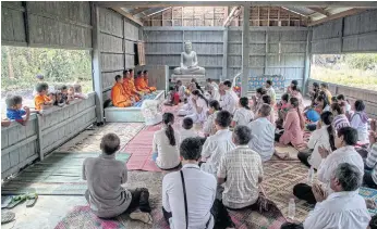  ??  ?? SAYING GOODBYE: Relatives and friends of a former Khmer Rouge member pray in front of a group of Buddhist monks while children watch during his funeral in Veal Hat village in Malai.
