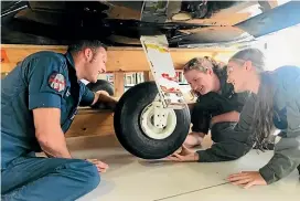  ?? MAXINE JACOBS/ STUFF ?? Flight Sergeant Brendon Pugh, left, shows Holly Inglis and Alexis Usal how to fit a wheel to a Grumman aircraft.