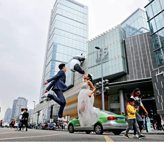  ?? VCG ?? 2 de octubre de 2018. Una pareja de recién casados salta, mientras en el fondo se ve la figura de un oso panda en la calle Chunxi, en Chengdu.