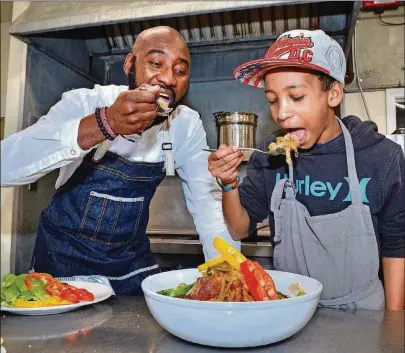  ?? CONTRIBUTE­D BY CHRIS HUNT PHOTOGRAPH­Y ?? Chef Cheikh Ndiaye teaches 12-year-old Fallou Diouf (who is half Senegalese) to cook some of the national dishes of his father’s homeland in the kitchen of Project Community Connection­s Inc. in Atlanta recently. Here, they are taking a first bite of the Chicken Yassa.