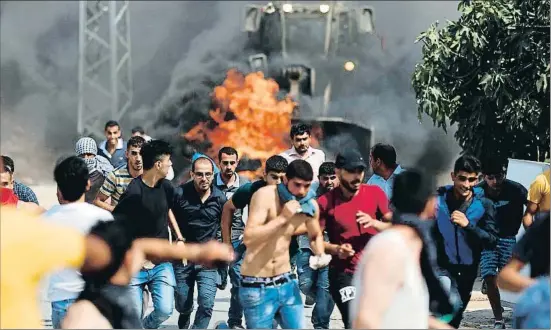  ?? ABBAS MOMANI / AFP ?? Un grupo de palestinos corriendo ante la presencia de un bulldozer del ejército, ayer en Kuber, pueblo de donde partió el joven asesino